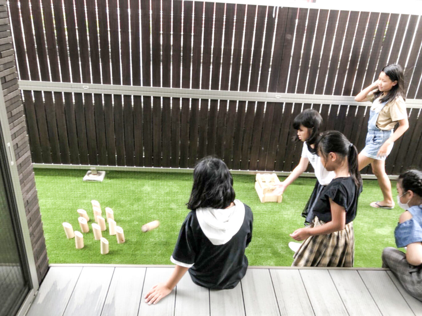 ウッドデッキに座って人工芝を敷いた庭で遊ぶ子ら