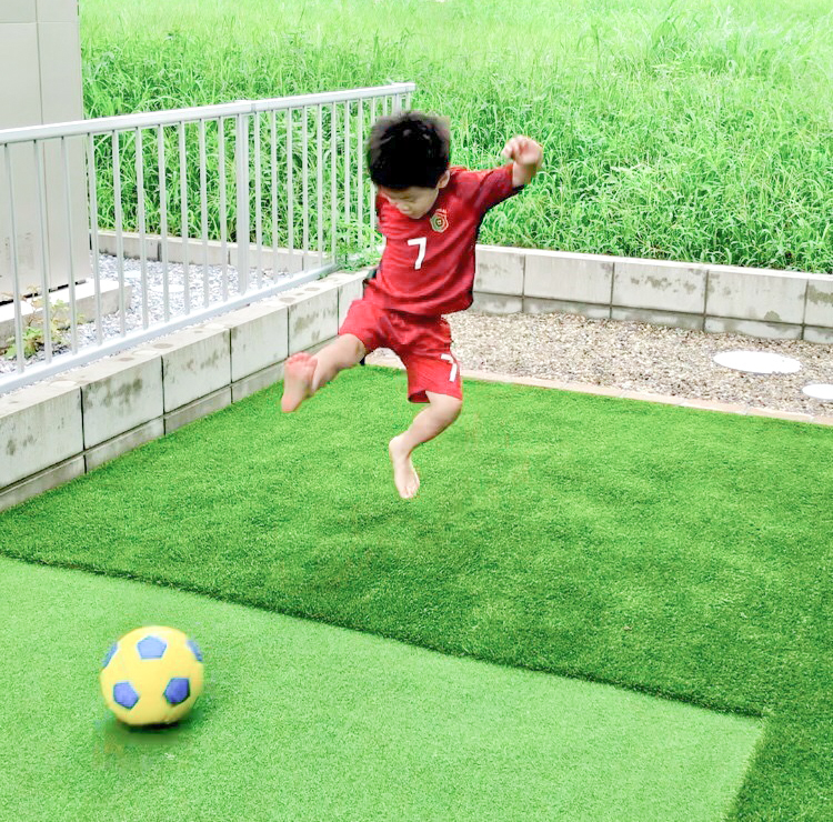 人工芝のお庭でサッカーをする少年